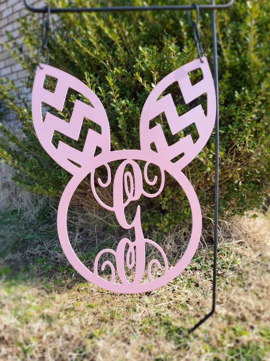 Outdoor Easter decor that is a metal garden flag shaped like a bunny with ears and the monogram in the middle.