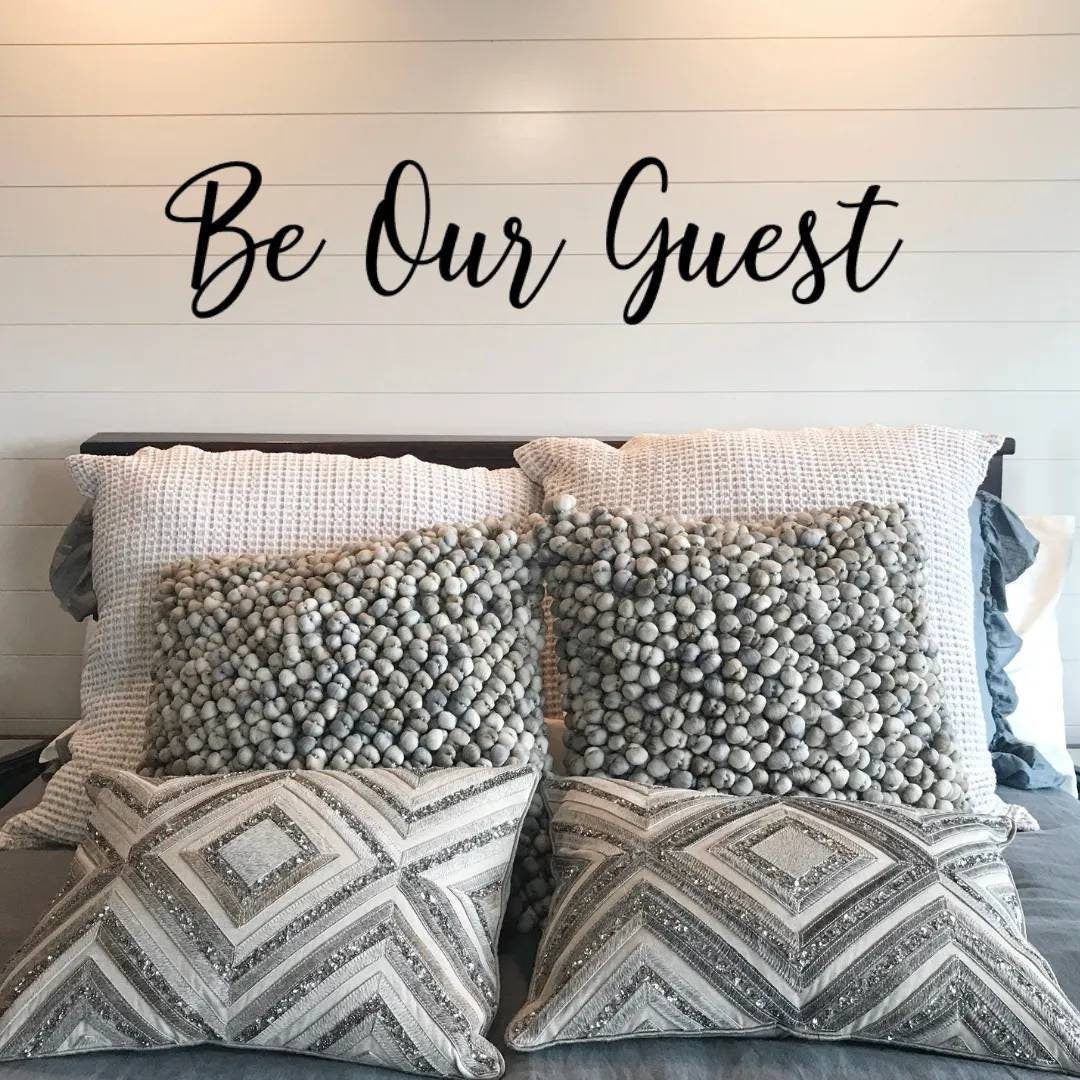 A farmhouse style guest bedroom with the metal words Be Our Guest above the bed.