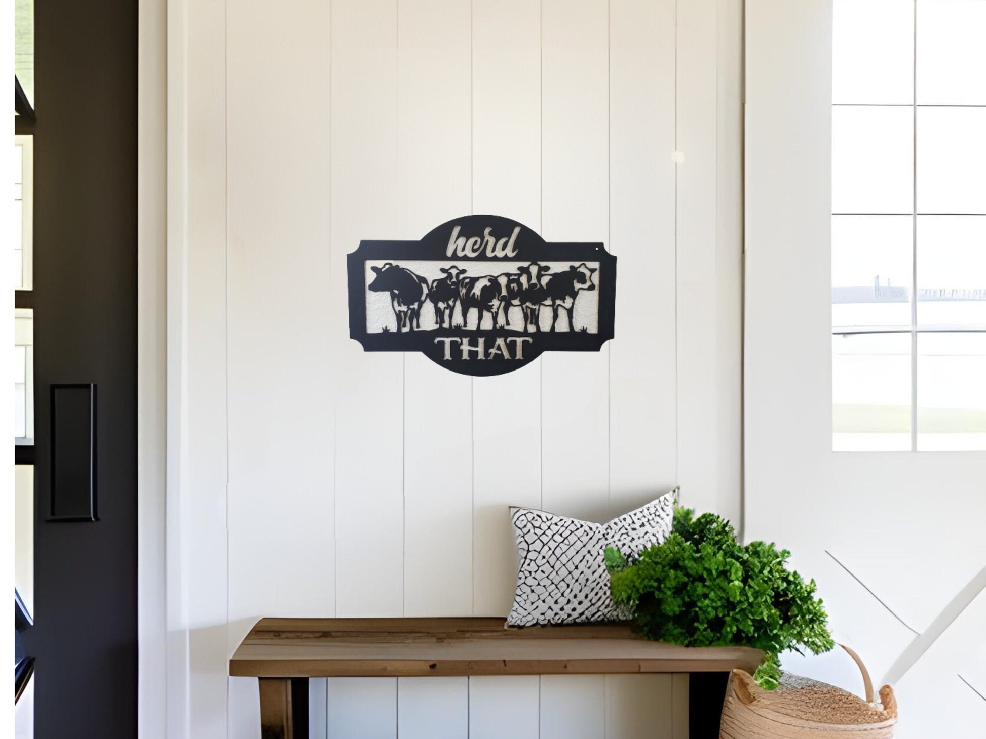 Metal sign that has cows and says herd that. It is hanging in a farmhouse decor home above a bench.