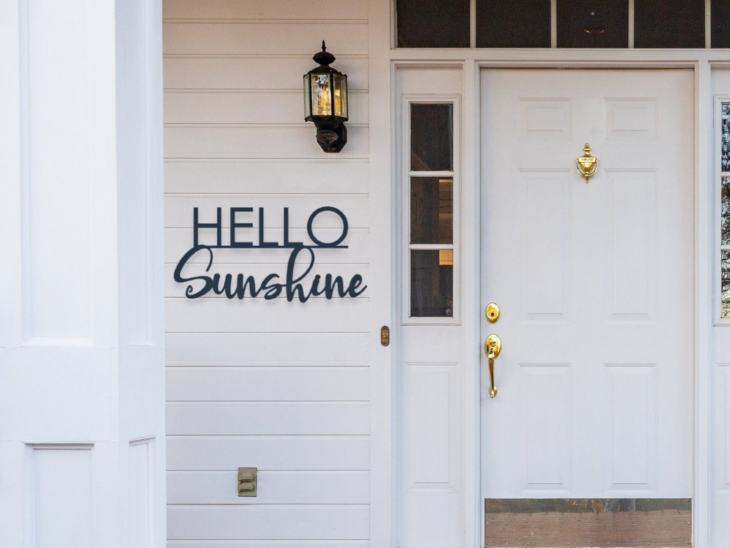 A metal sign on the front porch by the front door that says Hello Sunshine.