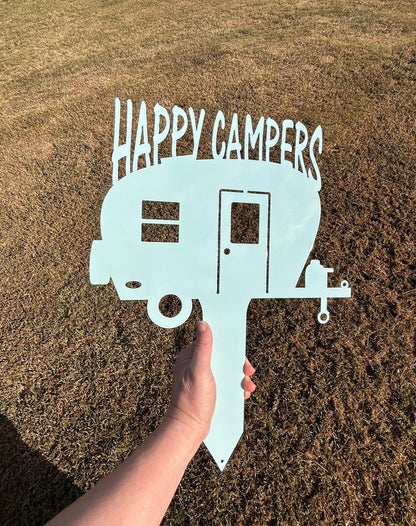 Metal yard art that is a yard stake that has a camper and over the camper it says Happy Camper. 