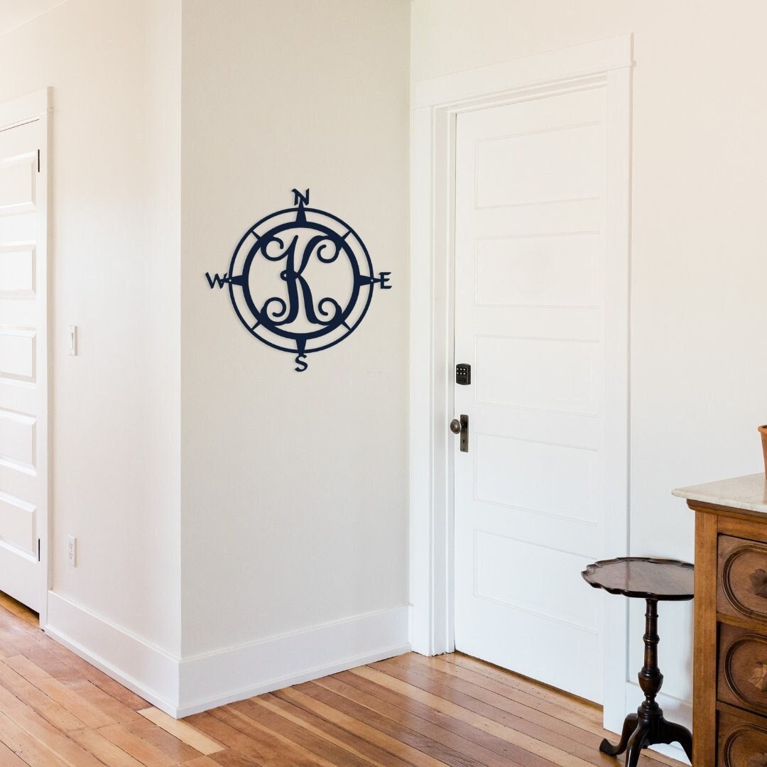 Metal Compass Sign that has a monogram initial in the middle. It is hanging on the entry way wall.