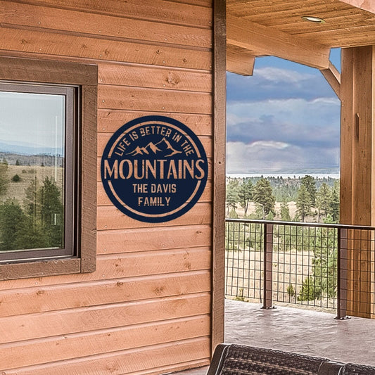 Mountain metal sign that is personalized at the bottom. It is hanging on the porch of a cabin.